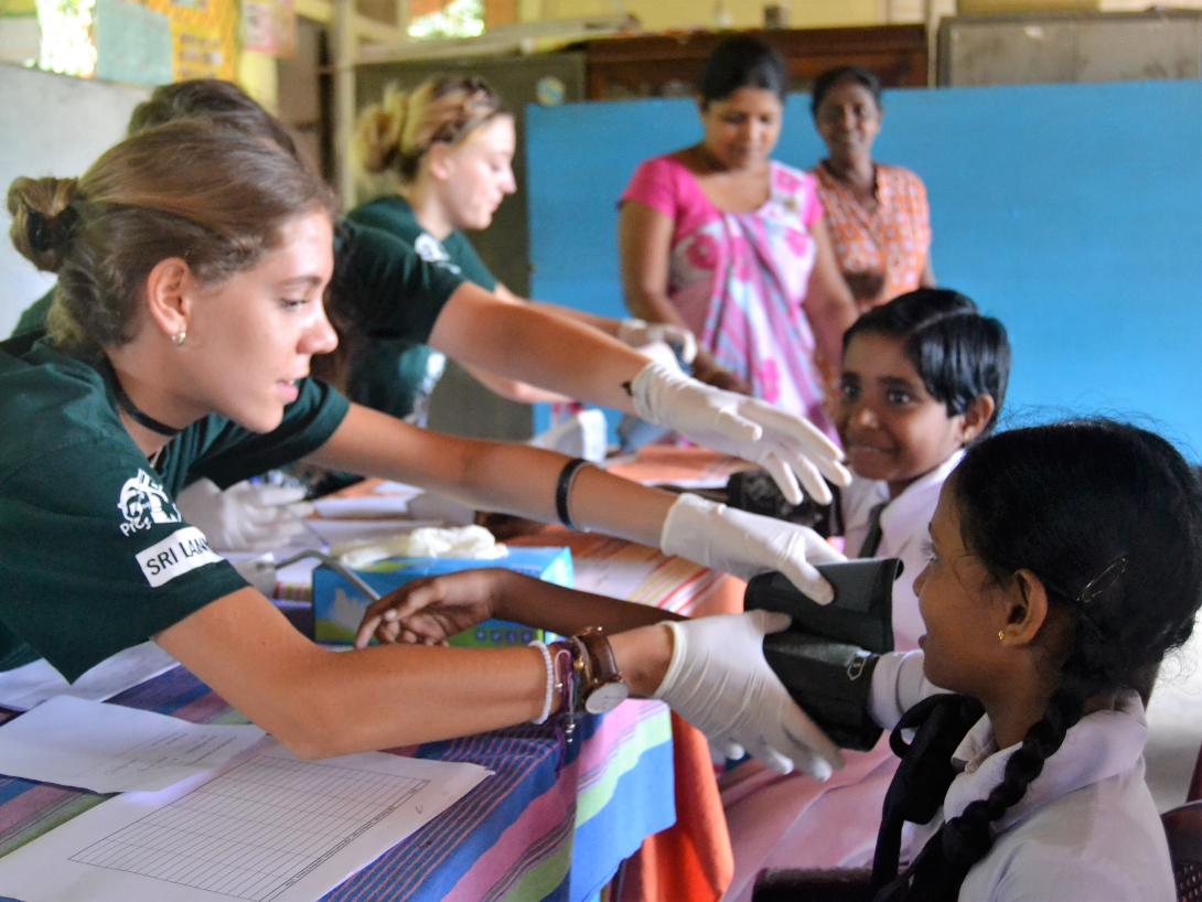 A group of clinical volunteers participate in a healthcare outreach at a school in Sri Lanka, Asia. A clinical volunteer abroad measures the blood pressure of a young child in Sri Lanka.